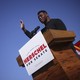 Herschel Walker stands at a lectern with his right hand in the air.