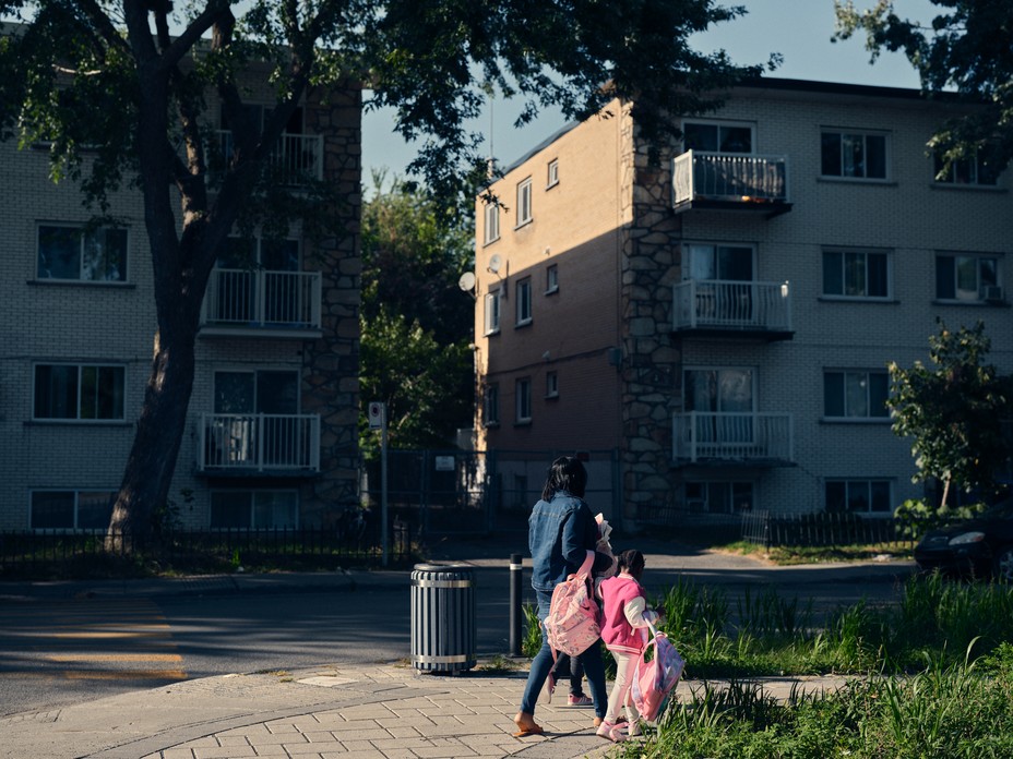 a woman and girl walk in front of apartment buildings