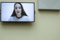 A TV screen showing the face of Oleksandra Matviychuk, as if on a video-call