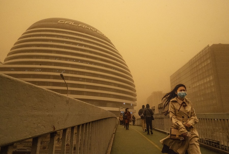 People walk past buildings under an eerie orange sky and low visibility.