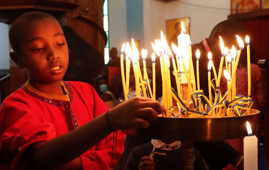 A boy lights a candle, set among a couple of dozen other candles, during a church service.