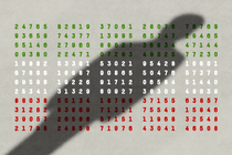A man's shadow falls over boxes of numbers that are color-coded to look like the Iranian flag, in green, white, and red