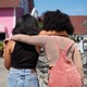 Friends stand with their arms around each other.