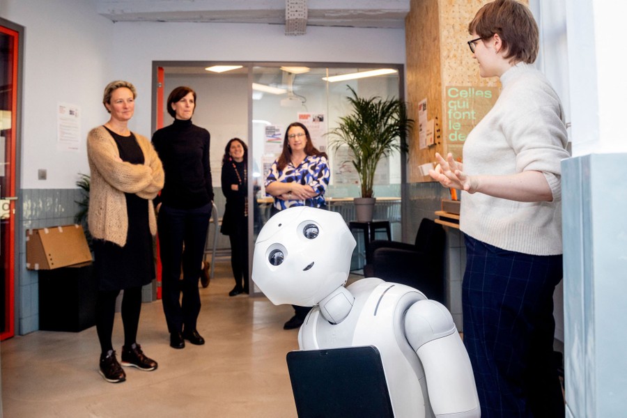 Five people stand and talk in a hallway as a small robot appears to look toward the camera.