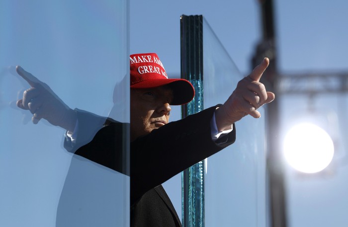 Donald Trump points his finger, and it reflects in the opposite direction on a pane of glass