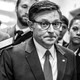 A black-and-white photo of Mike Johnson walking down a hallway, surrounded by other people