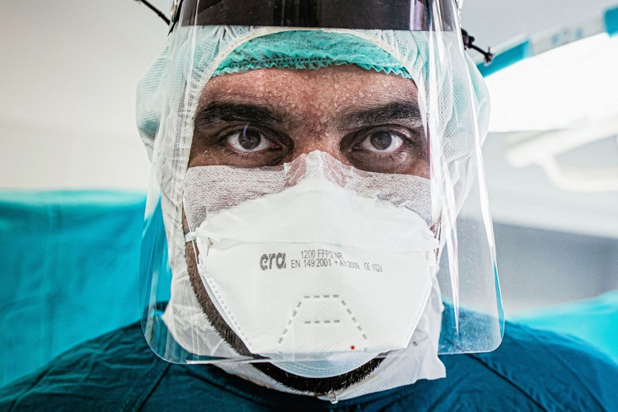 A portrait of a health-care worker wearing protective gear and sweating profusely.