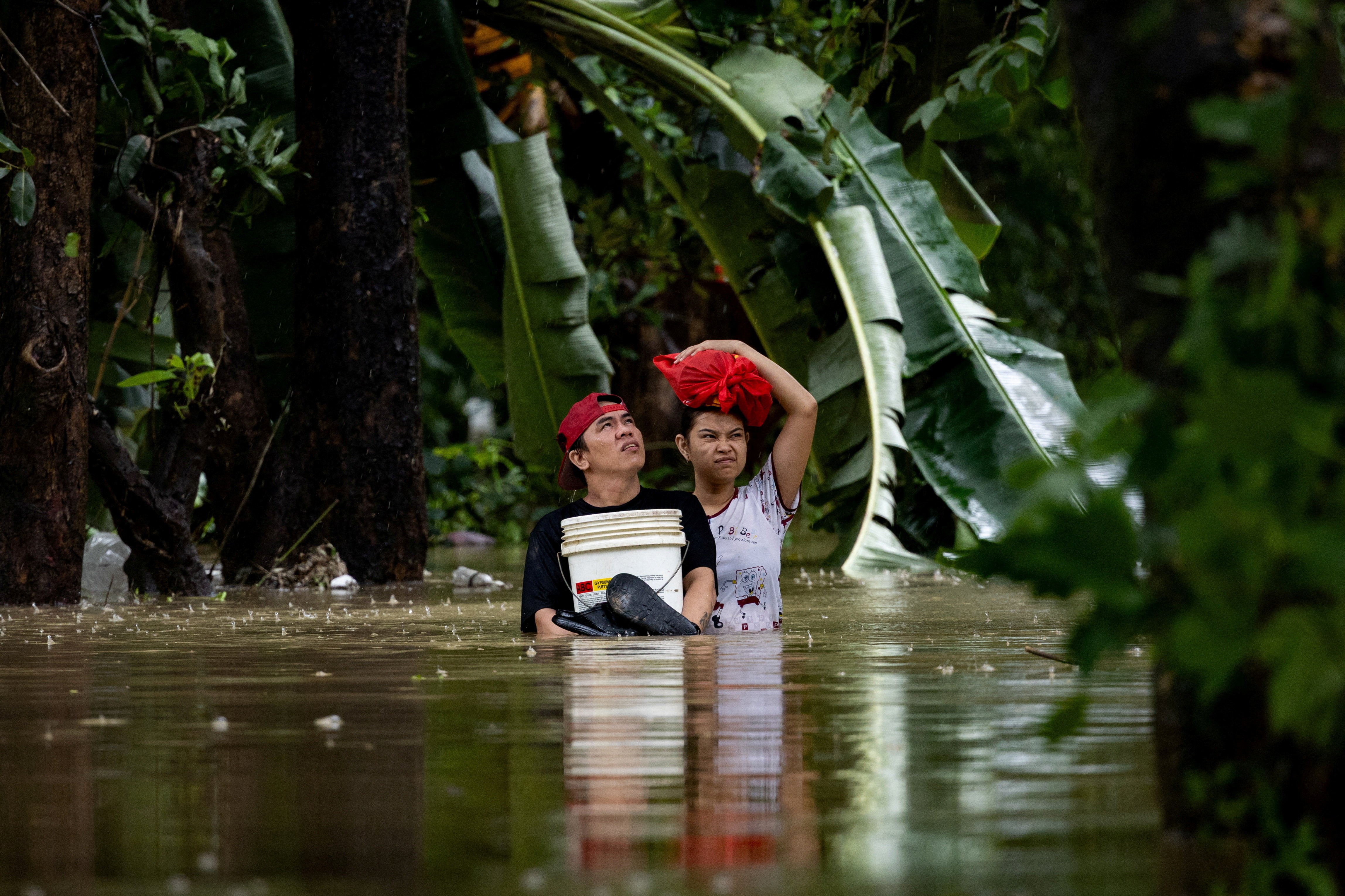 Two people carry belongings through belly-deep floodwater.