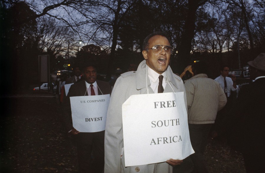 Harry Belafonte marches with others, wearing a sign that reads "Free South Africa."