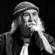 a black and white image of David Crosby in a knit cap with his hand to his chin