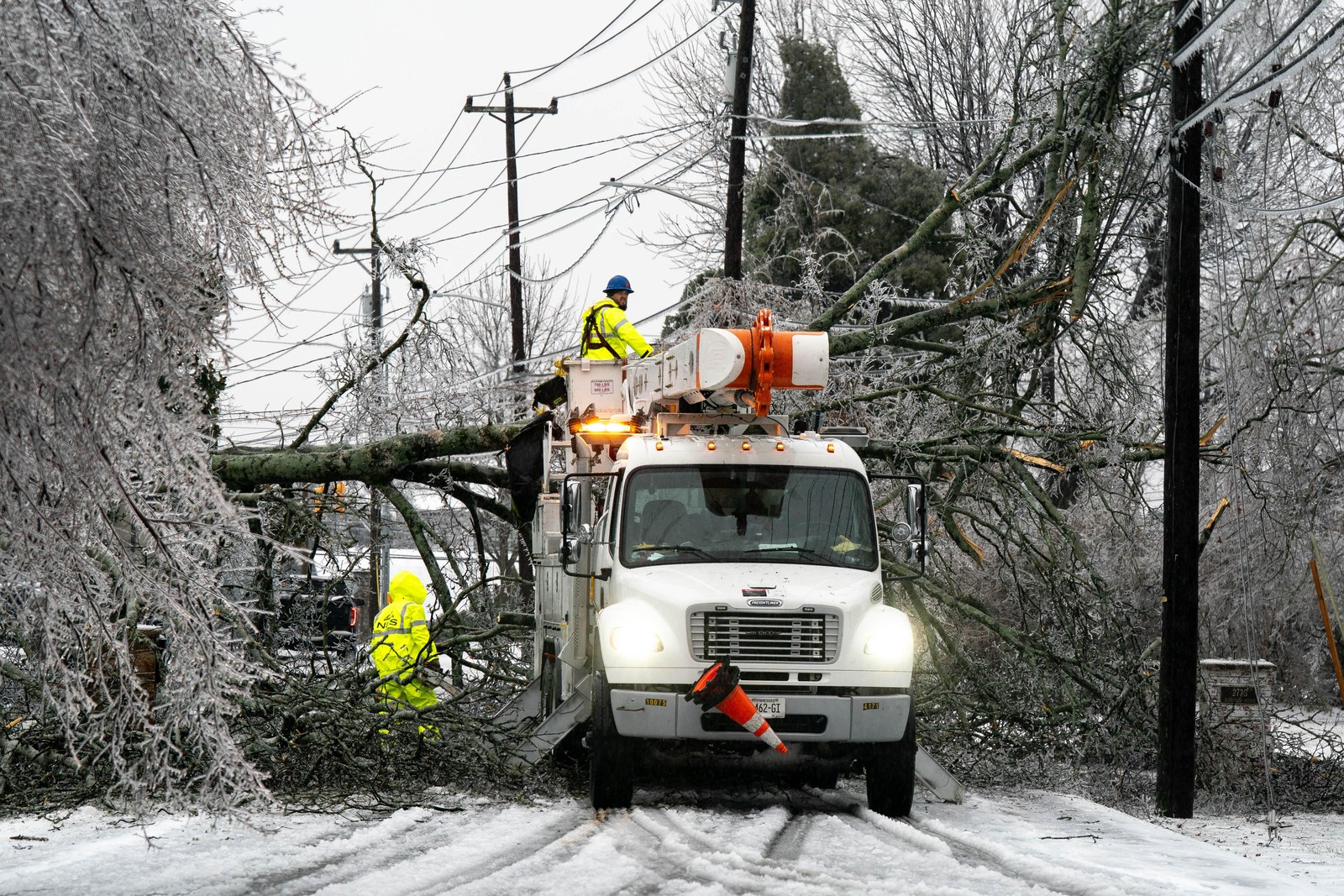 Workers try to restore power after a tree fell across powerlines during an ice storm.