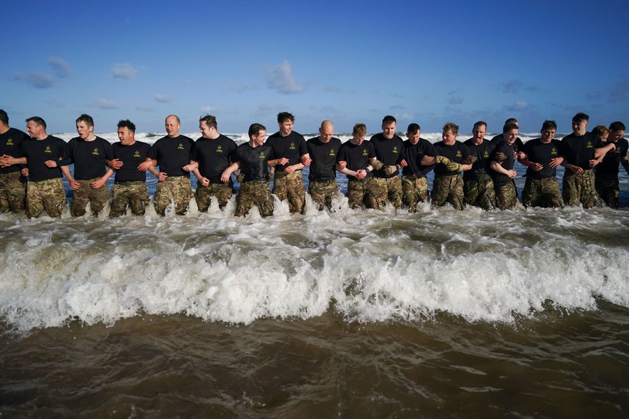 A couple of dozen soldiers stand side by side with arms linked, knee-deep in the surf near a beach.