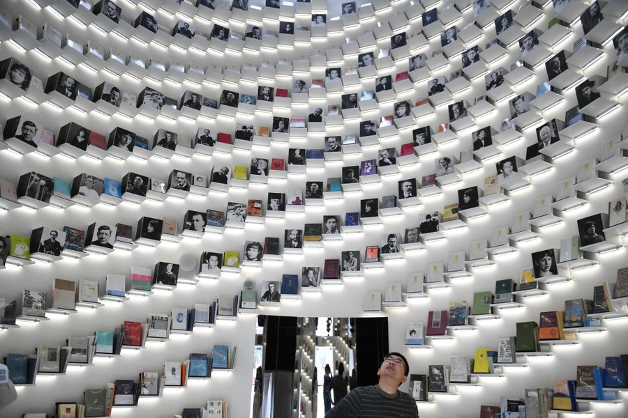 A person looks up at spiraling shelves of books arranged on a large curving wall.
