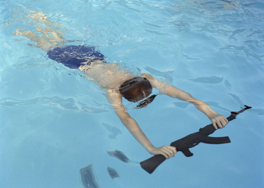 A young person swims in a pool while holding a weapon.
