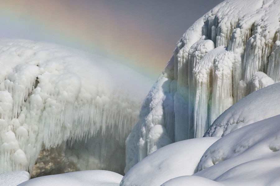 A slight rainbow is visible over large mounds of ice and icicles.