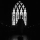 A black-and-white photo of the interior of an Episcopalian church. In the center of the image, a priest is backlit by sunlight coming through a stained glass window.