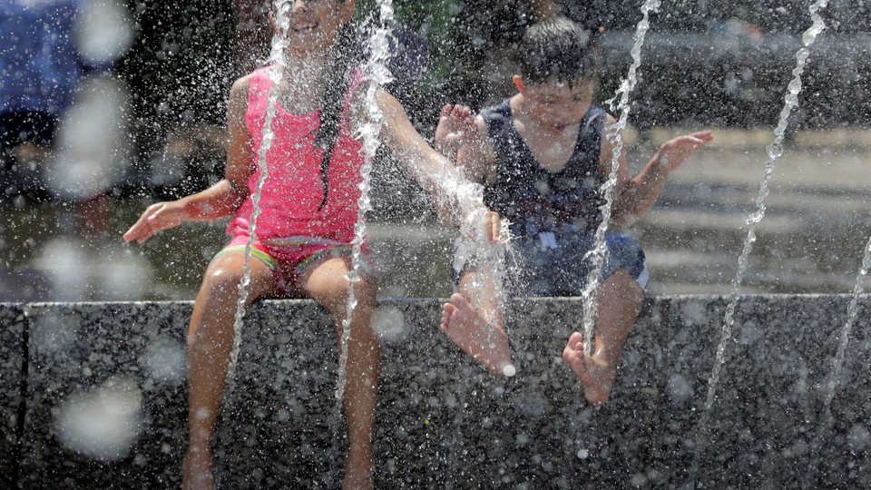 A girl in a pink tank top and a boy in a black tank top play in a fountain during a heat wave in Washington.