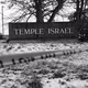 Black-and-white photograph of a sign reading “Temple Israel” behind police caution tape