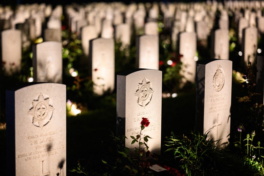 Many rows of illuminated military gravestones, one with a red flower in front of it