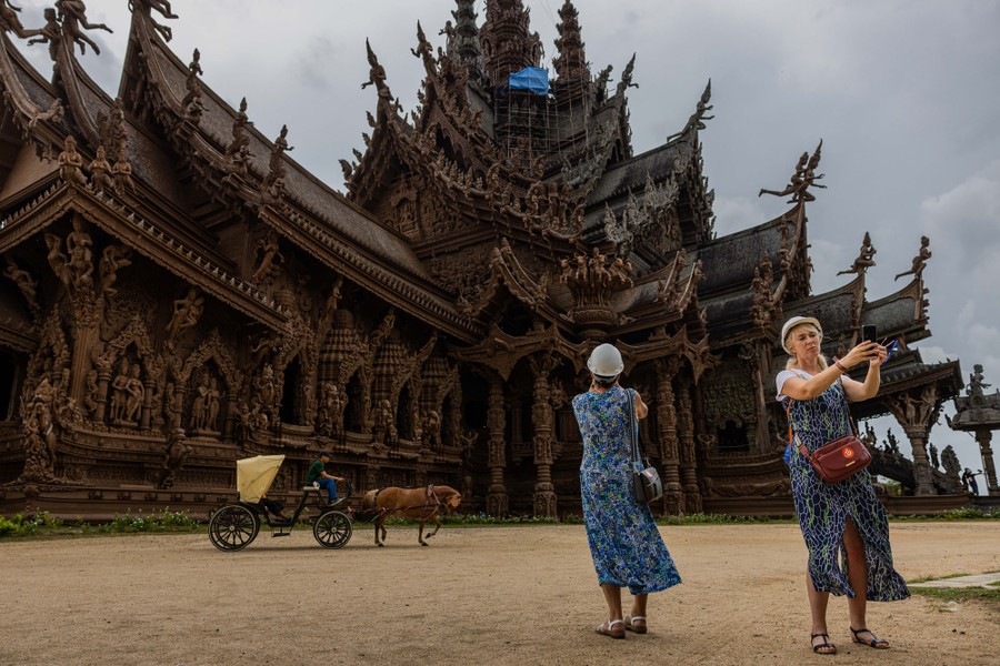 Tourists take photos in front of an ornate wooden structure covered in carvings and decorations.