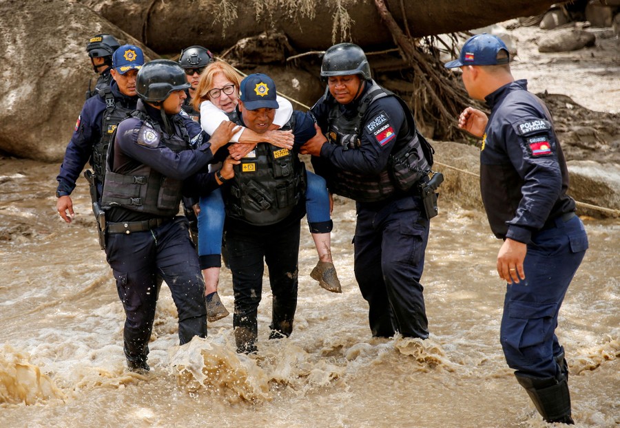 Several police officers help a woman cross a flooded area.