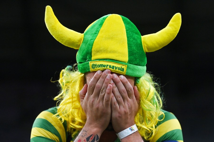 A person wearing a soft horned hat in Brazil's colors holds their hands over their face.