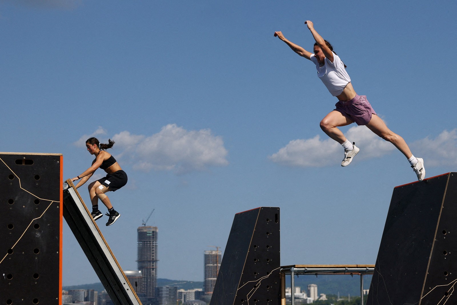 Two athletes leap and climb across an obstacle course during a parkour competition.