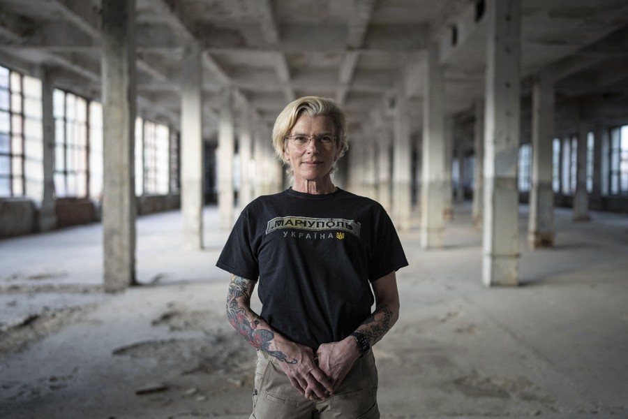 A woman stands inside a damaged building, posing for a portrait.