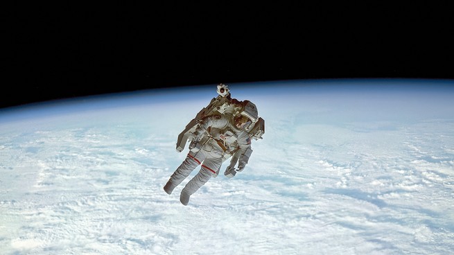 photo of astronaut on spacewalk isolated over luminous curved horizon of Earth against black