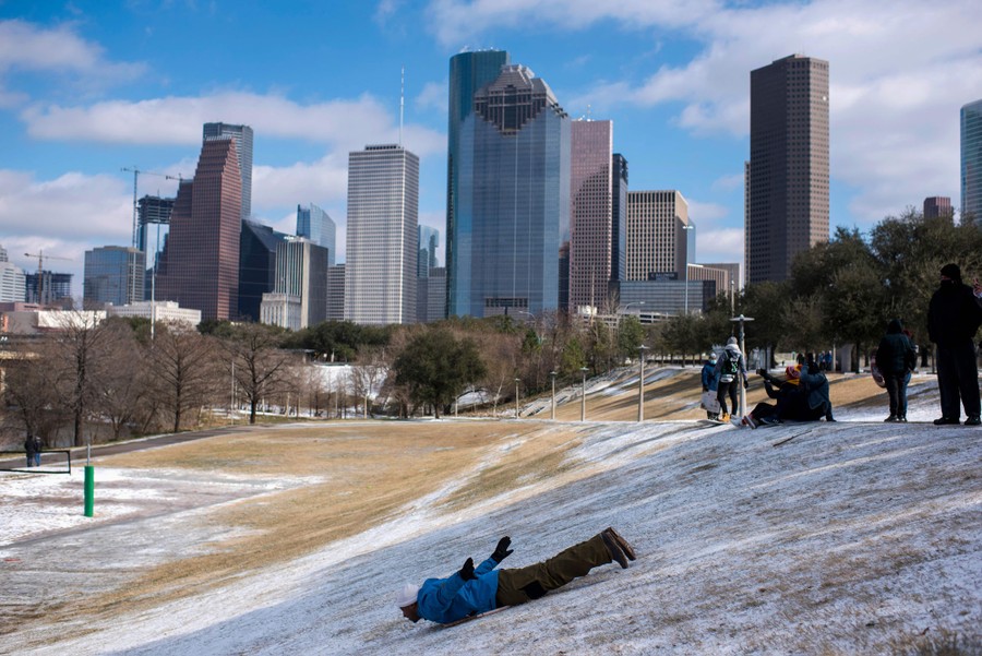 A man sleds on a light coating of snow in front of the buildings of downtown Houston.
