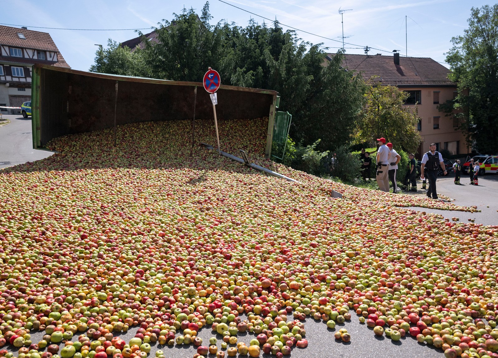 An overturned truck lies on its side, with a large load of apples spilled out onto a road.