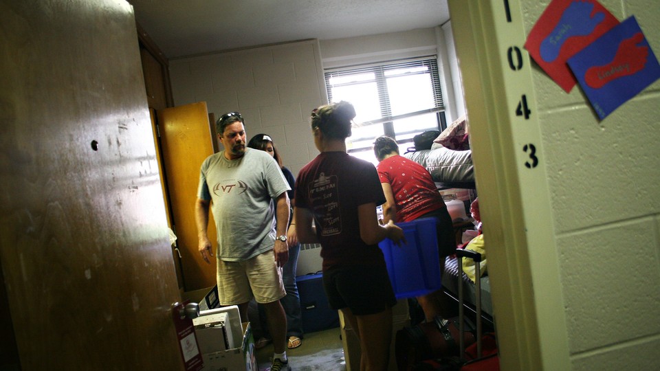 A family unpacks a student's luggage and furniture in a dorm room. 