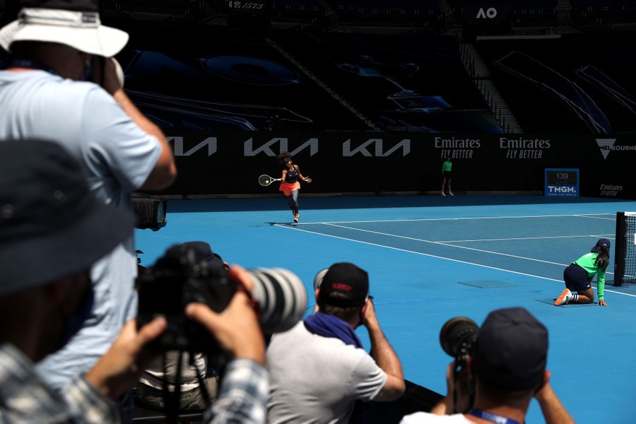 Several photographers point their lenses toward Naomi Osaka during gameplay.