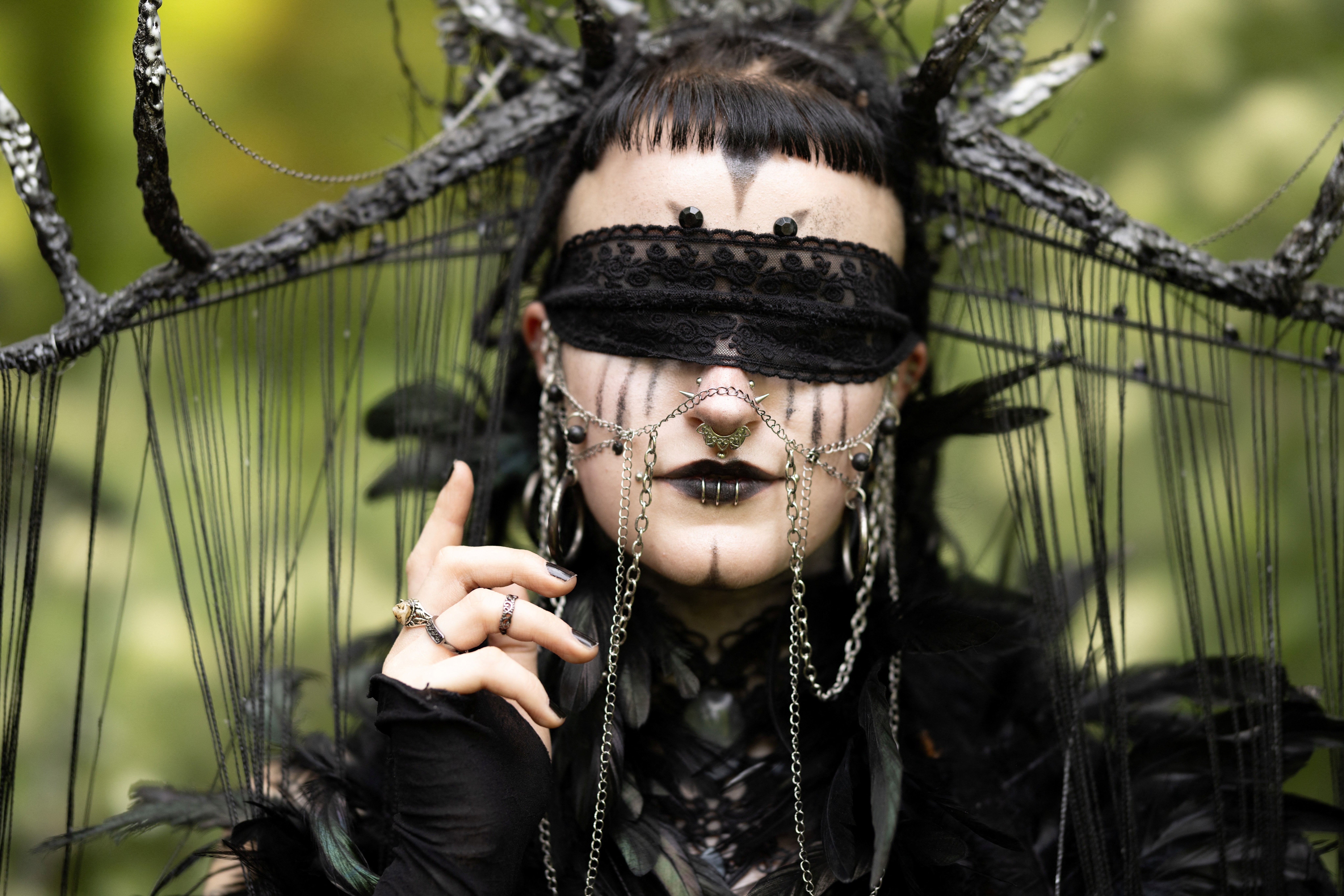 A person poses while wearing dark makeup and dark ornate clothing and accessories.