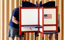Picture showing a circular voting booth and two voters whose faces are hidden behind the walls of the cubicles..