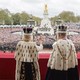 King Charles and Queen Camilla stand on the balcony at Buckingham Palace with their backs to the camera, facing the crowds at their coronation