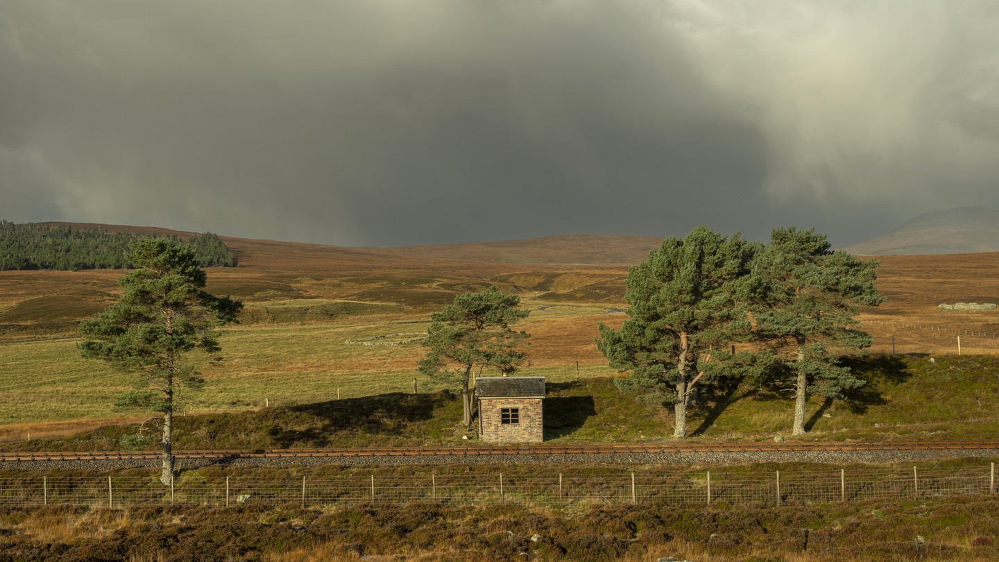 A small cottage stands below gray clouds with sun peeking through.
