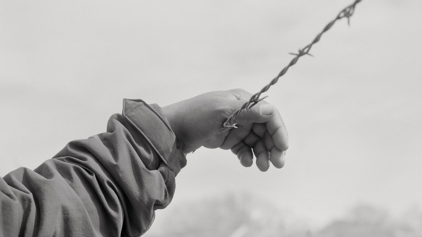 Raul Rodriguez's hand rested on barbed wire in black and white.
