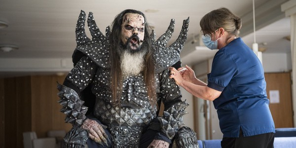 A heavy metal singer in costume receives a vaccine dose from a nurse.