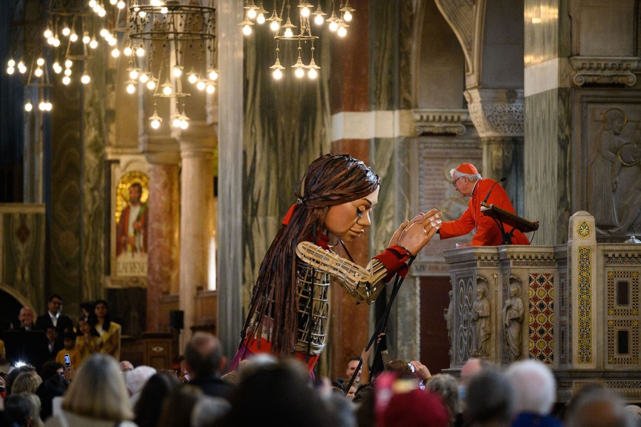A giant puppet reaches out to a cardinal in a cathedral in London.