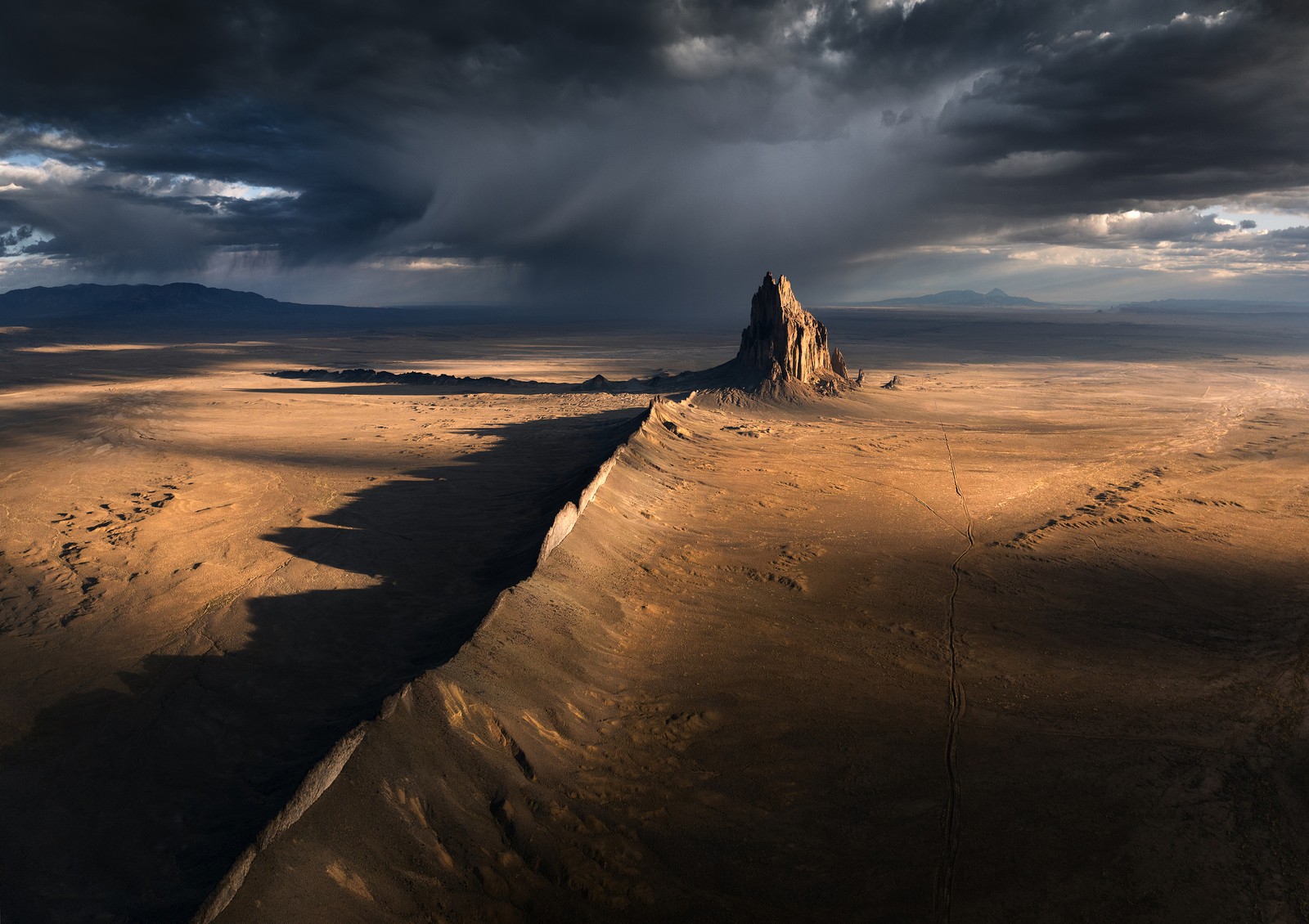 An aerial view of a desert landscape with a tall, rocky spire beneath a stormy sky