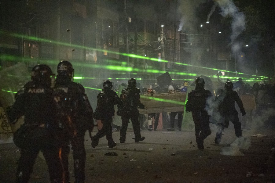 Lasers shine above a large group of protesters and riot police.