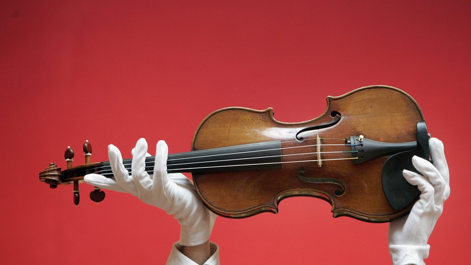 A person wearing white gloves holds up a violin