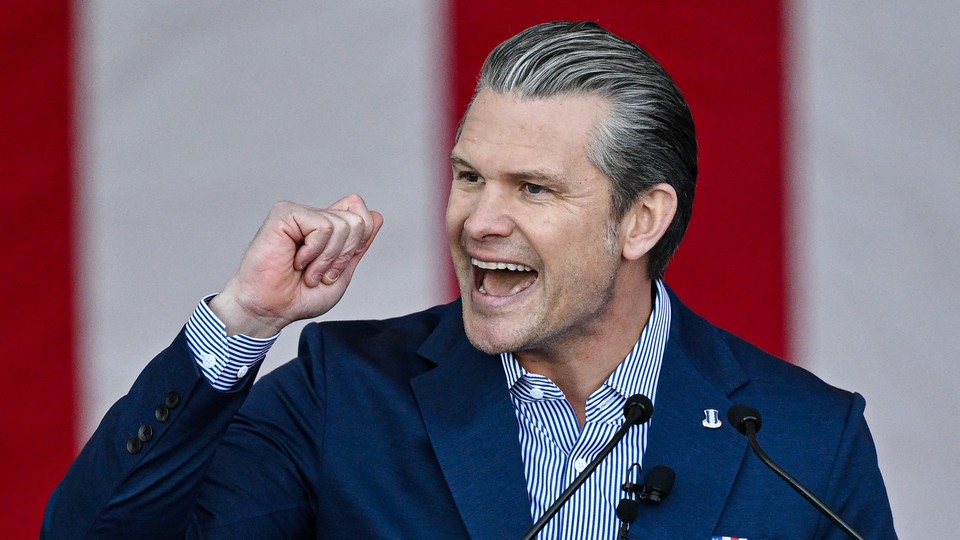 Pete Hegseth talks behind microphones while he makes a fist with his right hand
