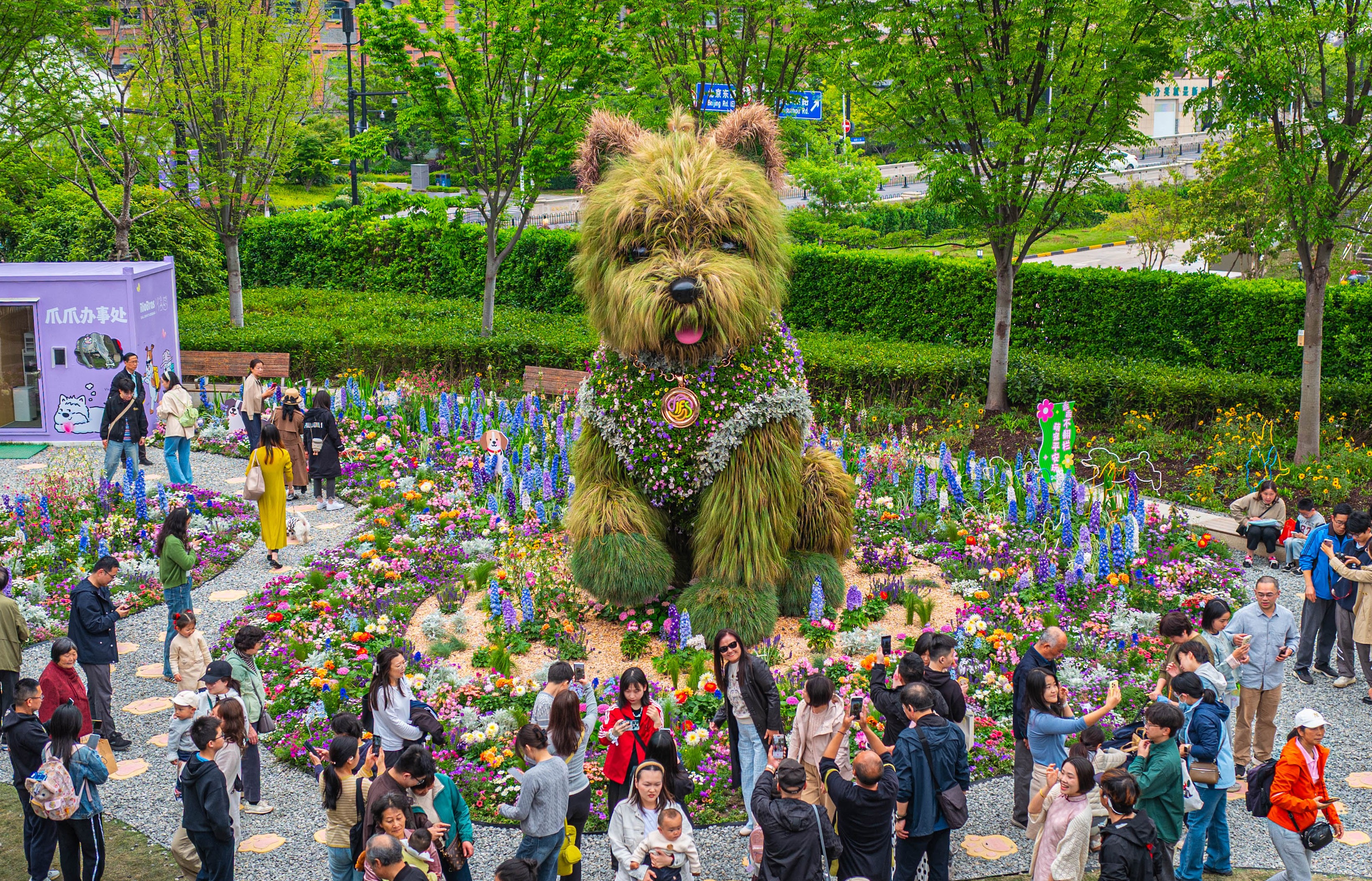 Visitors gather around a tall sculpture of a dog made of flowers and greenery.