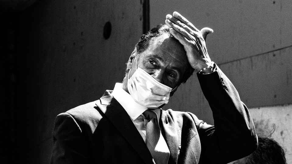 Andrew Cuomo wipes his hand across his forehead while wearing a mask