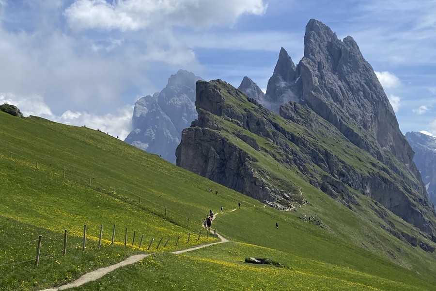 Hikers walk on a path toward a spectacular mountaintop.