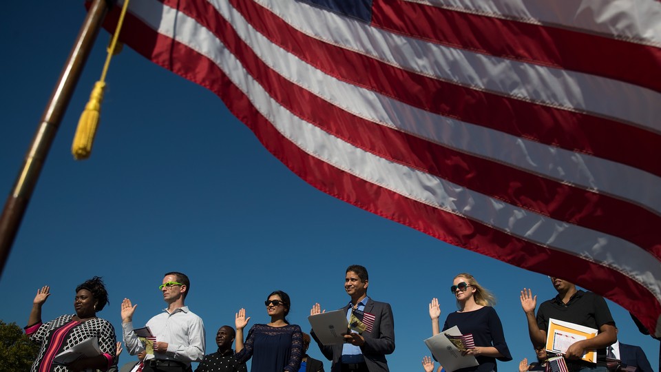 Framed by an American flag, immigrants raise their right hands and take the oath of allegiance during a naturalization ceremony.