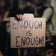 A hand holds up a sign that reads "Enough Is Enough!"