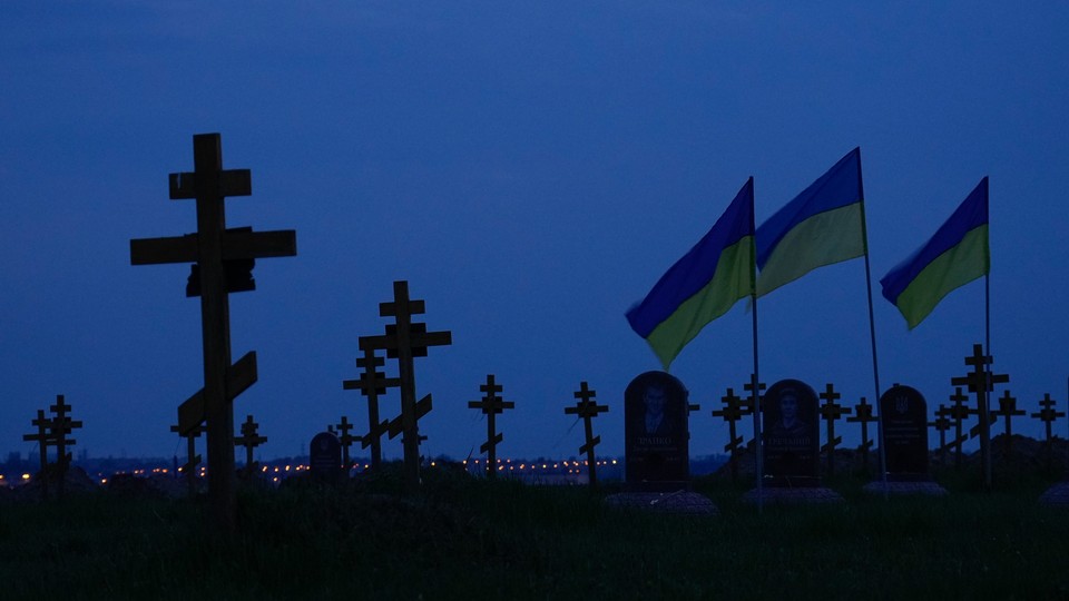 Photo of a cemetery with crosses and Ukrainian flags visible against a dark sky